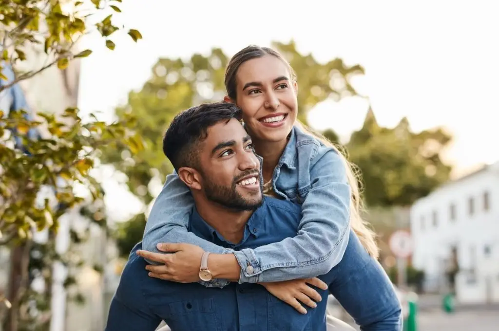 Travel, piggyback and happy couple with love in the city on a walk while on a romantic date. Happiness, smile and young man and woman having fun, walking and bonding in the town street on a vacation.