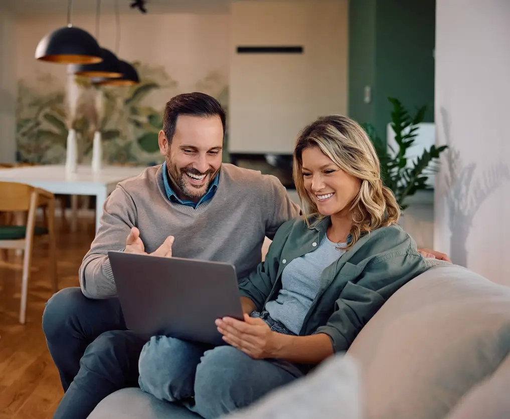 Happy couple using computer while relaxing on the sofa at home.